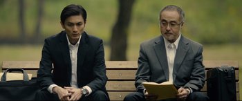Movie still from “Shin Godzilla” (2016), directed by Shinji Higuchi – Two men sitting on a park bench reading; Medium shot, Low angle
