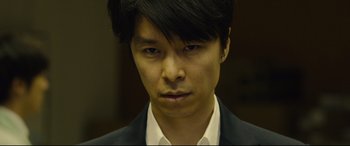 Movie still from “Shin Godzilla” (2016), directed by Shinji Higuchi – A person wearing a suit and tie; Close Up shot, Low angle