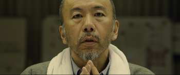 Movie still from “Shin Godzilla” (2016), directed by Shinji Higuchi – A person wearing a robe; Close Up shot, Low angle