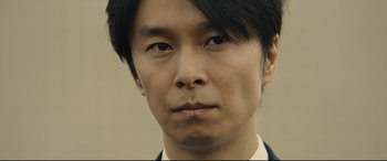Movie still from “Shin Godzilla” (2016), directed by Shinji Higuchi – A person wearing a suit and tie; Extreme Close Up shot, Low angle