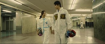 Movie still from “Shin Godzilla” (2016), directed by Shinji Higuchi – A man and a woman in white coveralls holding hands; Medium shot, Low angle