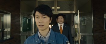 Movie still from “Shin Godzilla” (2016), directed by Shinji Higuchi – Two men in suits and ties standing next to each other in front of a building; Close Up shot, Low angle