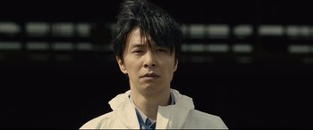 Movie still from “Shin Godzilla” (2016), directed by Shinji Higuchi – A man with a black hair and a white jacket; Close Up shot, Low angle