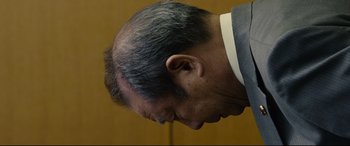 Movie still from “Shin Godzilla” (2016), directed by Shinji Higuchi – A person wearing a suit and tie; Close Up shot, Low angle