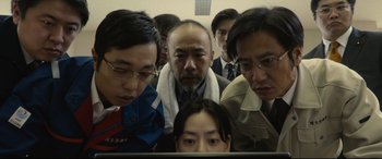 Movie still from “Shin Godzilla” (2016), directed by Shinji Higuchi – A group of people standing around a computer screen; Medium shot, Low angle
