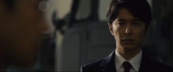 Movie still from “Shin Godzilla” (2016), directed by Shinji Higuchi – A person wearing a suit and tie; Close Up shot, Low angle