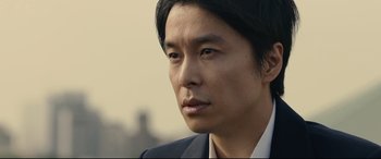 Movie still from “Shin Godzilla” (2016), directed by Shinji Higuchi – A person wearing a suit and tie; Close Up shot, Low angle