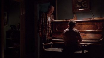 Movie still from “Shine” (1996), directed by Scott Hicks – A man standing in front of a piano in a living room; Wide shot, Over the shoulder angle