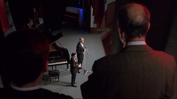 Movie still from “Shine” (1996), directed by Scott Hicks – A man and a woman standing in front of a microphone on a stage; Wide shot, High angle
