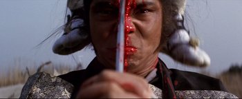 Movie still from “Shogun Assassin” (1980), directed by Kenji Misumi – A man with blood on his face holding a knife in front of his face; Extreme Close Up shot, Low angle