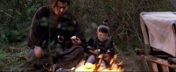 Movie still from “Shogun Assassin” (1980), directed by Kenji Misumi – A man and a boy sitting next to a fire; Medium shot, Over the shoulder angle