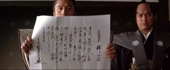 Movie still from “Shogun Assassin” (1980), directed by Kenji Misumi – A man holding up a sheet of paper with chinese writing on it; Close Up shot, Low angle