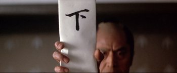 Movie still from “Shogun Assassin” (1980), directed by Kenji Misumi – A man holding up a piece of paper with the letter t written on it; Extreme Close Up shot, Overhead angle