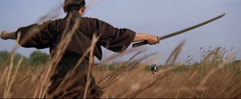 Movie still from “Shogun Assassin” (1980), directed by Kenji Misumi – A person holding a sword in a field; Wide shot, Low angle