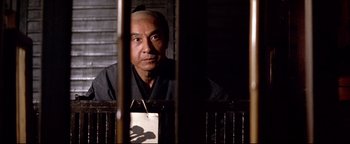Movie still from “Shogun Assassin” (1980), directed by Kenji Misumi – A man sitting in front of a wooden fence; Close Up shot, Low angle