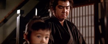 Movie still from “Shogun Assassin” (1980), directed by Kenji Misumi – A man and a boy in a black kimono; Close Up shot, Low angle