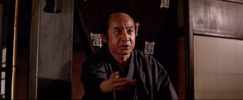 Movie still from “Shogun Assassin” (1980), directed by Kenji Misumi – An older man in a black shirt is talking; Close Up shot, Low angle