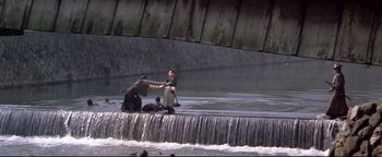 Movie still from “Shogun Assassin” (1980), directed by Kenji Misumi – Two men are holding hands in front of a waterfall; Extreme Wide shot, High angle