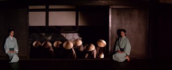 Movie still from “Shogun Assassin” (1980), directed by Kenji Misumi – A group of people wearing hats sitting in a room; Wide shot, Low angle