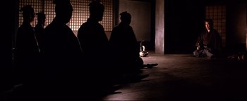 Movie still from “Shogun Assassin” (1980), directed by Kenji Misumi – Two people sitting on the ground in a dark room; Wide shot, Low angle