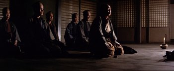 Movie still from “Shogun Assassin” (1980), directed by Kenji Misumi – A group of people sitting on the ground in front of a building; Wide shot, Low angle