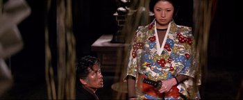 Movie still from “Shogun Assassin” (1980), directed by Kenji Misumi – A man and a woman standing next to each other holding a guitar; Medium shot, Low angle