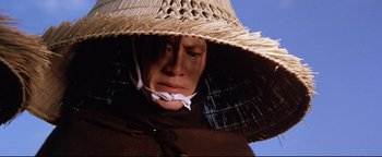 Movie still from “Shogun Assassin” (1980), directed by Kenji Misumi – A man wearing a straw hat with a white ribbon around his mouth; Close Up shot, Low angle