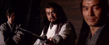 Movie still from “Shogun Assassin” (1980), directed by Kenji Misumi – A man with a long black hair holding a sword in his hand; Medium shot, Low angle