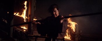 Movie still from “Shogun Assassin” (1980), directed by Kenji Misumi – A man holding two swords in front of a fire; Medium shot, Low angle