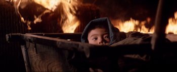 Movie still from “Shogun Assassin” (1980), directed by Kenji Misumi – A young child peeking out from behind a fire pit; Close Up shot, High angle