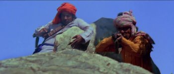 Movie still from “Sholay” (1975), directed by Ramesh Sippy – A man playing a musical instrument while another man takes a picture; Medium shot, Low angle