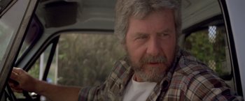 Movie still from “Short Circuit” (1986), directed by John Badham – An older man in a plaid shirt sitting in a car; Close Up shot, Low angle