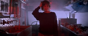 Movie still from “Short Circuit” (1986), directed by John Badham – A woman in a dark room smiling for the camera; Medium shot, Low angle