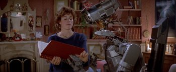 Movie still from “Short Circuit” (1986), directed by John Badham – A woman standing next to a robot in a living room; Medium shot, Over the shoulder angle