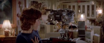 Movie still from “Short Circuit” (1986), directed by John Badham – A woman is looking at a camera on a table; Close Up shot, Over the shoulder angle