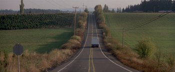 Movie still from “Short Circuit” (1986), directed by John Badham – A truck driving down a road near a lush green field; Extreme Wide shot, High angle