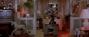 Movie still from “Short Circuit” (1986), directed by John Badham – A robot is standing in a living room with a plant; Wide shot, High angle