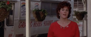 Movie still from “Short Circuit” (1986), directed by John Badham – A woman standing in front of a building with flowers hanging from it; Medium shot, Over the shoulder angle