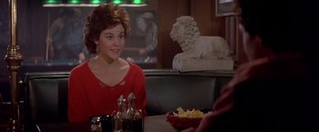 Movie still from “Short Circuit” (1986), directed by John Badham – A woman sitting at a table in front of a lion statue; Medium shot, Over the shoulder angle