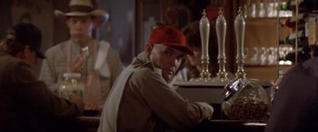 Movie still from “Short Circuit” (1986), directed by John Badham – A man sitting at a table in front of a bar; Close Up shot, Over the shoulder angle