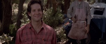 Movie still from “Short Circuit” (1986), directed by John Badham – A man smiling while holding a skateboard in a forest; Close Up shot, Low angle