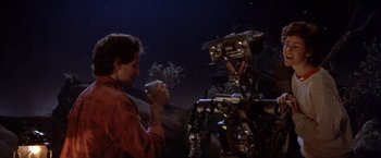 Movie still from “Short Circuit” (1986), directed by John Badham – A man standing in front of a robot; Medium shot, Over the shoulder angle