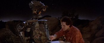 Movie still from “Short Circuit” (1986), directed by John Badham – A man sitting in front of a computer with a robot; Medium shot, High angle