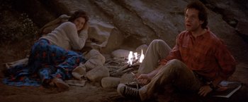 Movie still from “Short Circuit” (1986), directed by John Badham – A couple of people sitting on the ground next to a fire; Wide shot, High angle
