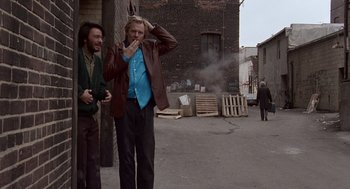 Movie still from “Short Circuit 2” (1988), directed by Kenneth Johnson – Two men standing on a side walk in front of a brick building; Wide shot, Over the shoulder angle
