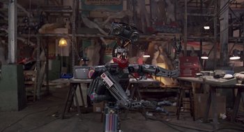 Movie still from “Short Circuit 2” (1988), directed by Kenneth Johnson – A robot is sitting on top of a table; Wide shot, Low angle