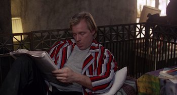 Movie still from “Short Circuit 2” (1988), directed by Kenneth Johnson – A man sitting in a chair reading a newspaper; Medium shot, Low angle