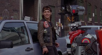 Movie still from “Short Circuit 2” (1988), directed by Kenneth Johnson – A man standing next to a car on the side of the road; Medium shot, Low angle