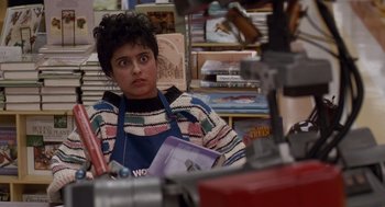 Movie still from “Short Circuit 2” (1988), directed by Kenneth Johnson – A woman sitting at a table in front of books; Medium shot, Over the shoulder angle