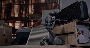 Movie still from “Short Circuit 2” (1988), directed by Kenneth Johnson – An old video camera sitting on top of a wooden table; Wide shot, Low angle